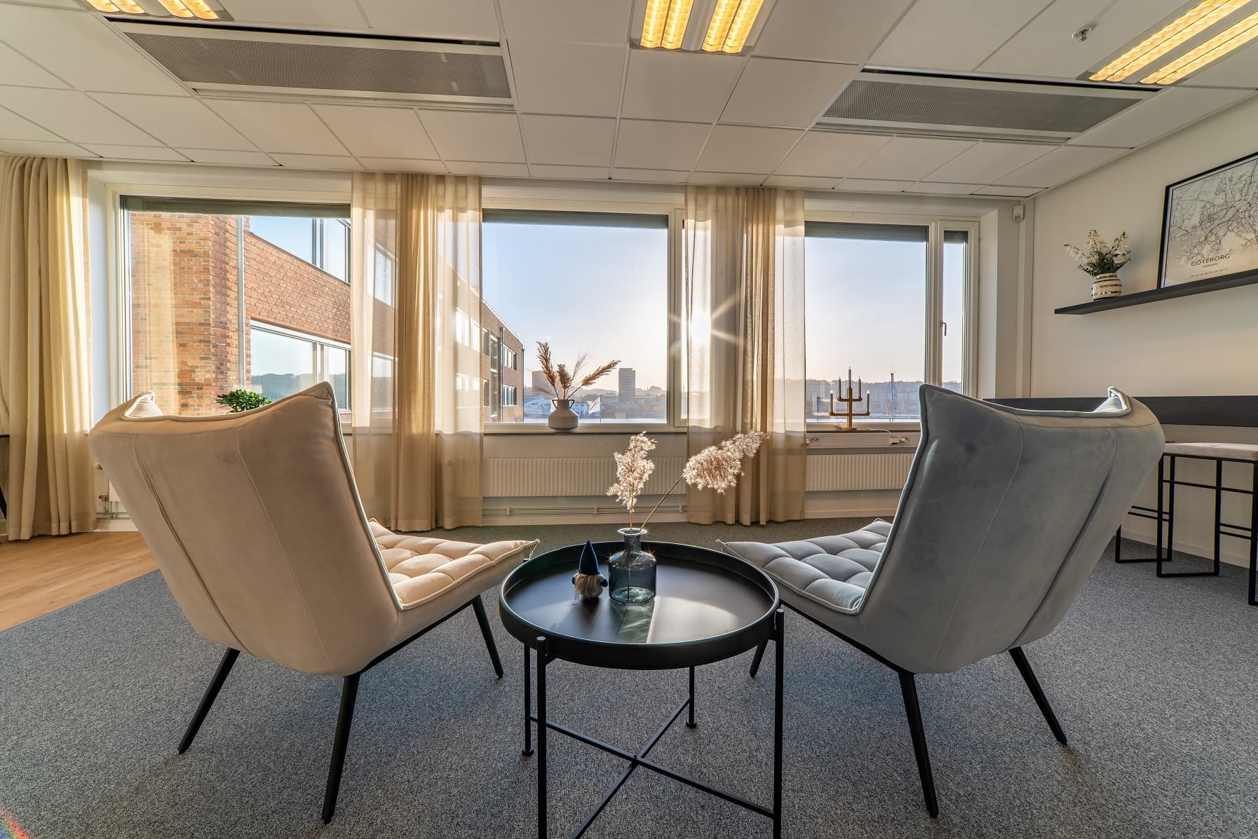 Lounge hos Seaside Office Hotels med fåtöljer mot fönstret och utsikt över staden